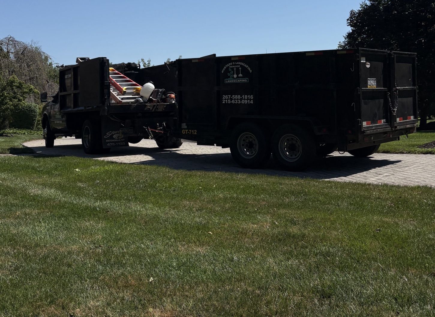 Hurtado's dump truck and trailer with the company logo on a paver driveway