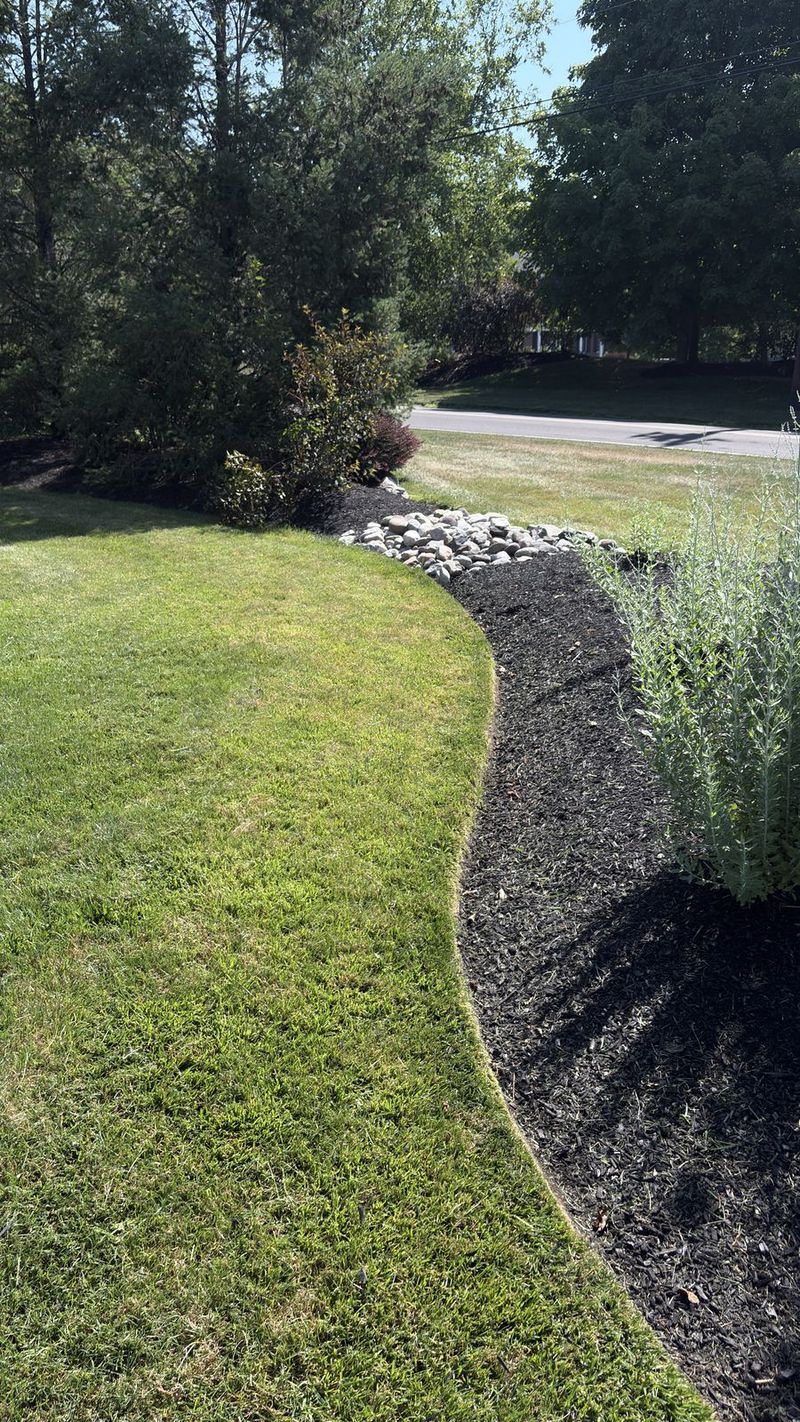 Black mulch bed with river rock and a clean edge against the lawn
