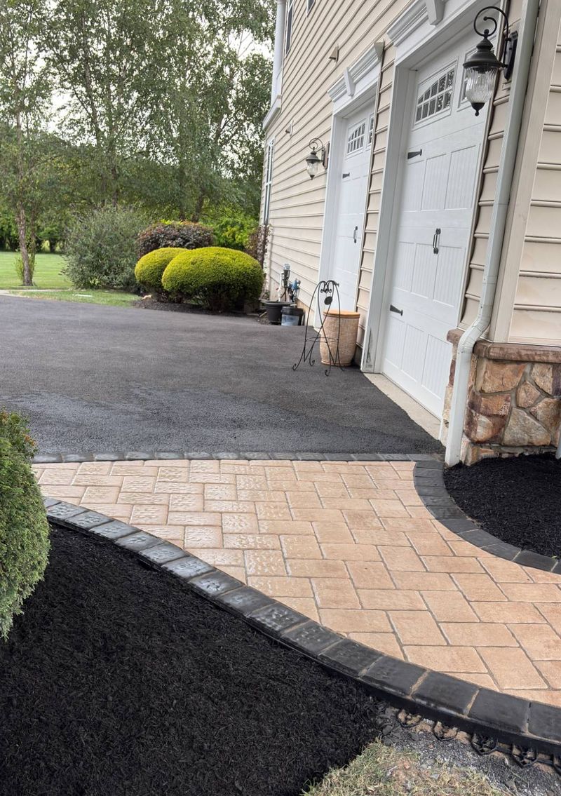 Paver walkway meeting the driveway apron at a two-car garage, edged with charcoal cobble